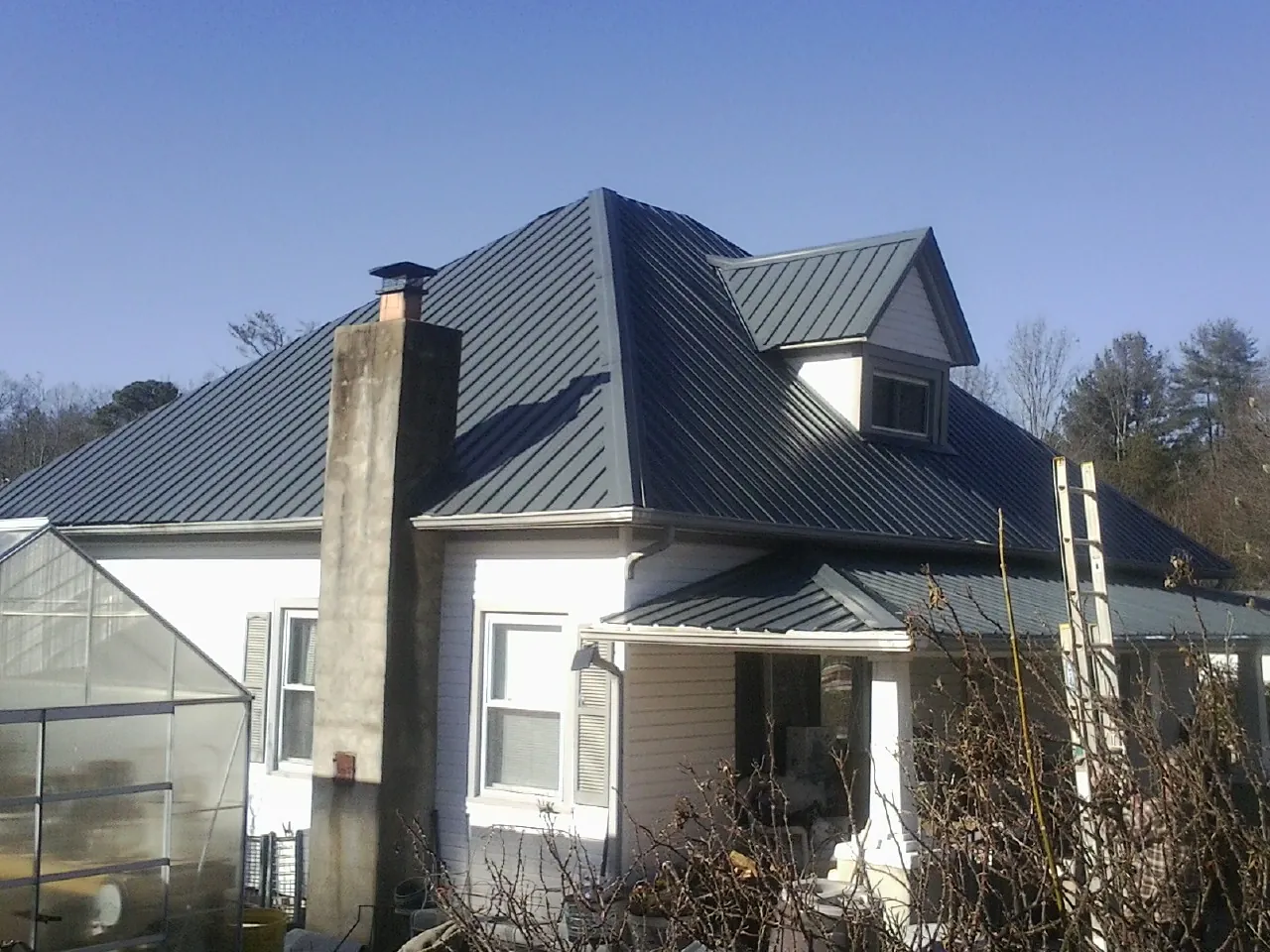 Dark blue standing seam metal roof on a white farmhouse with dormer — Slate & Tile Roof Repair by Roofing Brothers in Metaline