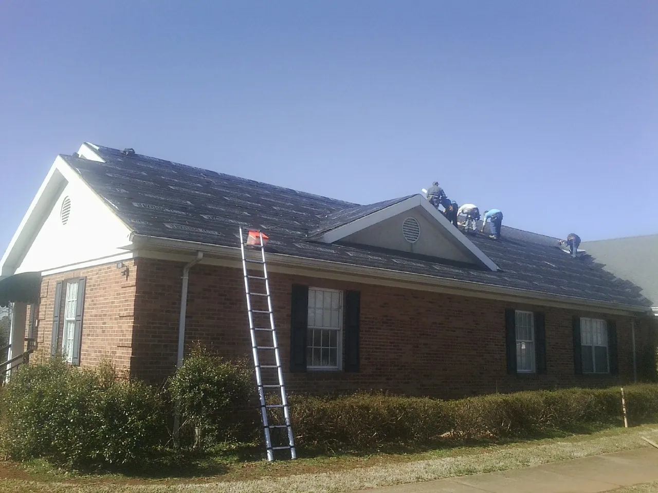Crew tearing shingles off a brick ranch roof with a ladder set — Metal Roof Repair work by our crew in Metaline