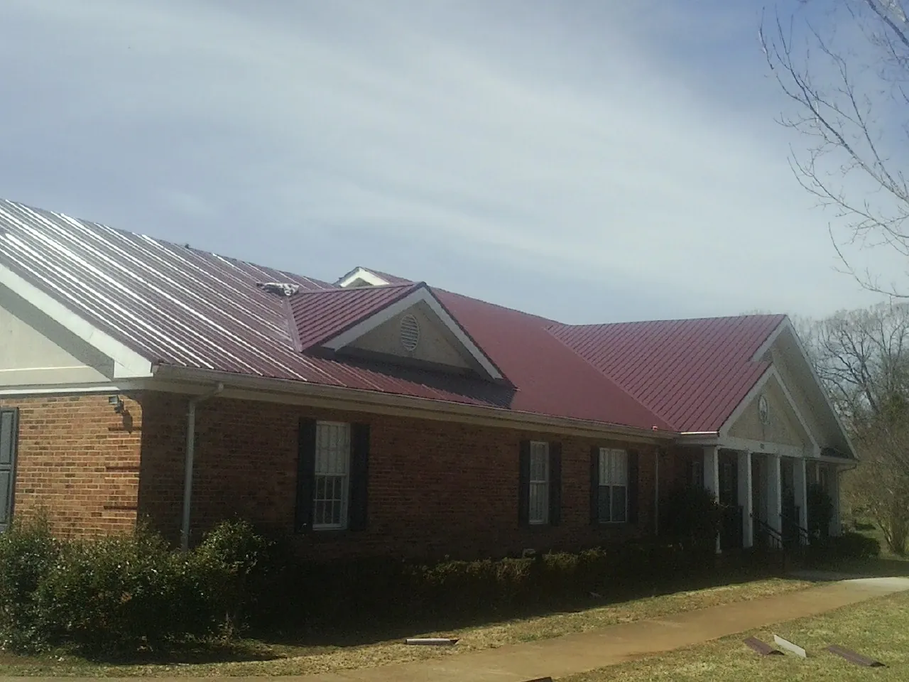 Red metal roof with gabled entries on a long brick building, from a Hail Damage Roof Repair job in Metaline
