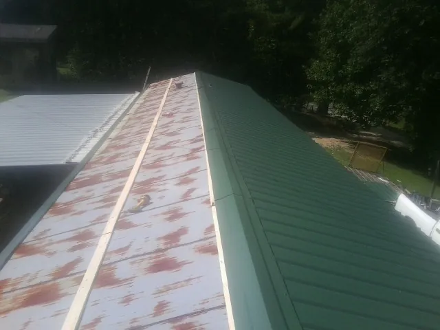 Old rusted panels beside newly installed green metal roofing — Wind Damage Roof Repair by Roofing Brothers in Metaline