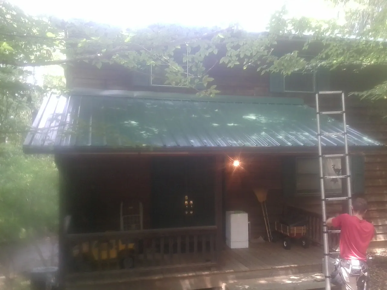 Worker on a ladder at the green porch roof of a wooded cabin in Metaline