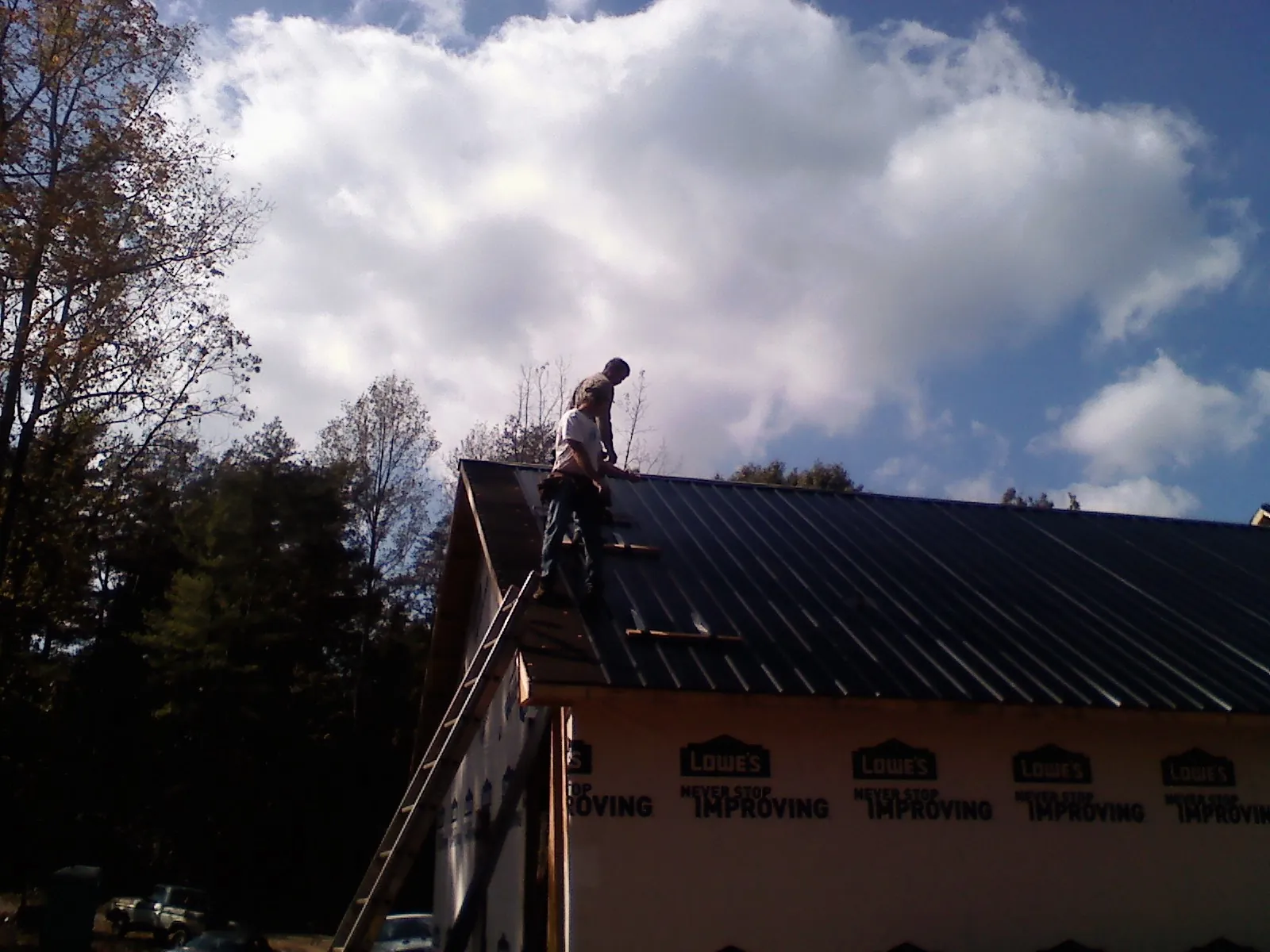 Roofer fastening dark metal panels high against a cloudy sky, from a Roof Inspection job in Metaline